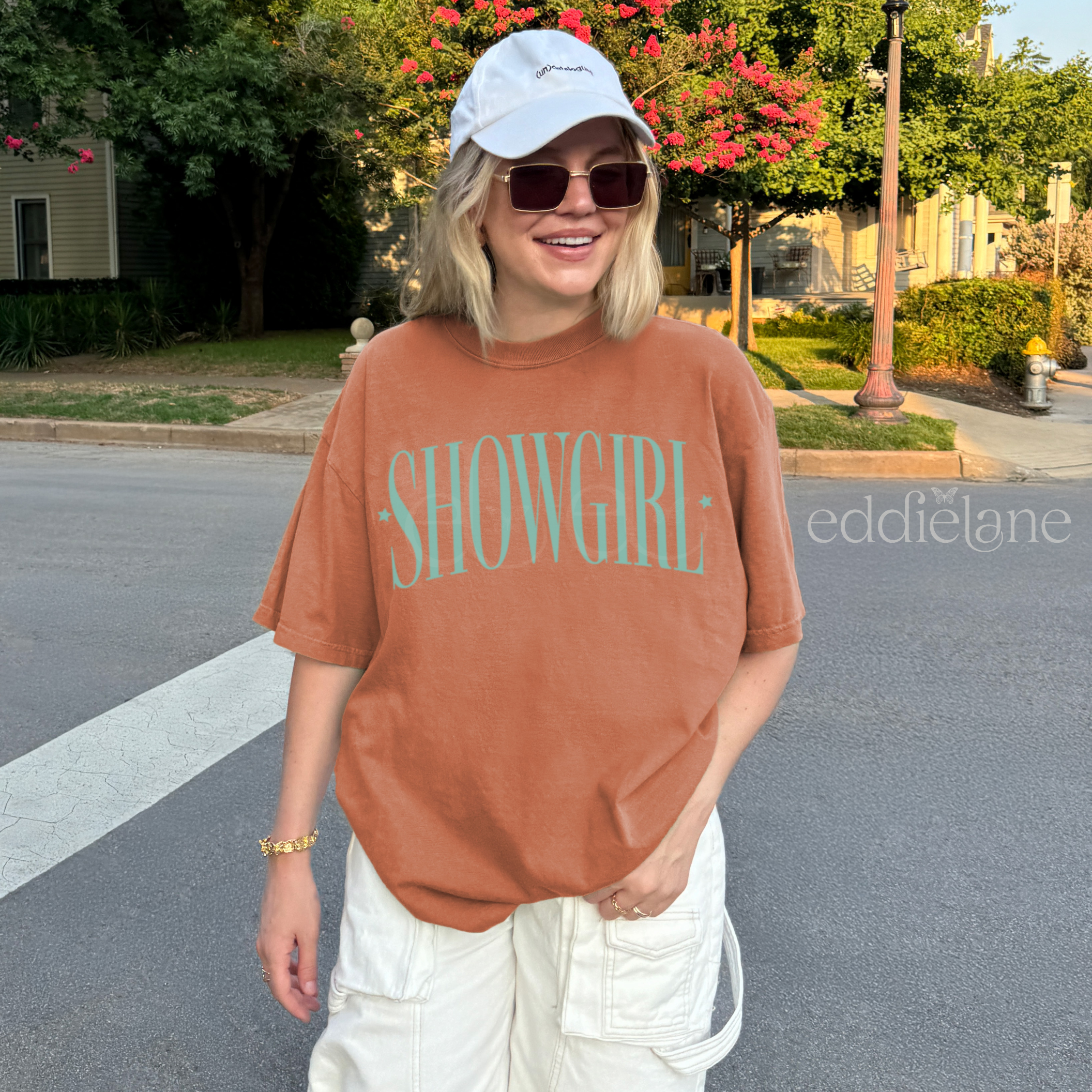 Woman wearing an orange comfort colors graphic tee that says 'SHOWGIRL' with two small stars