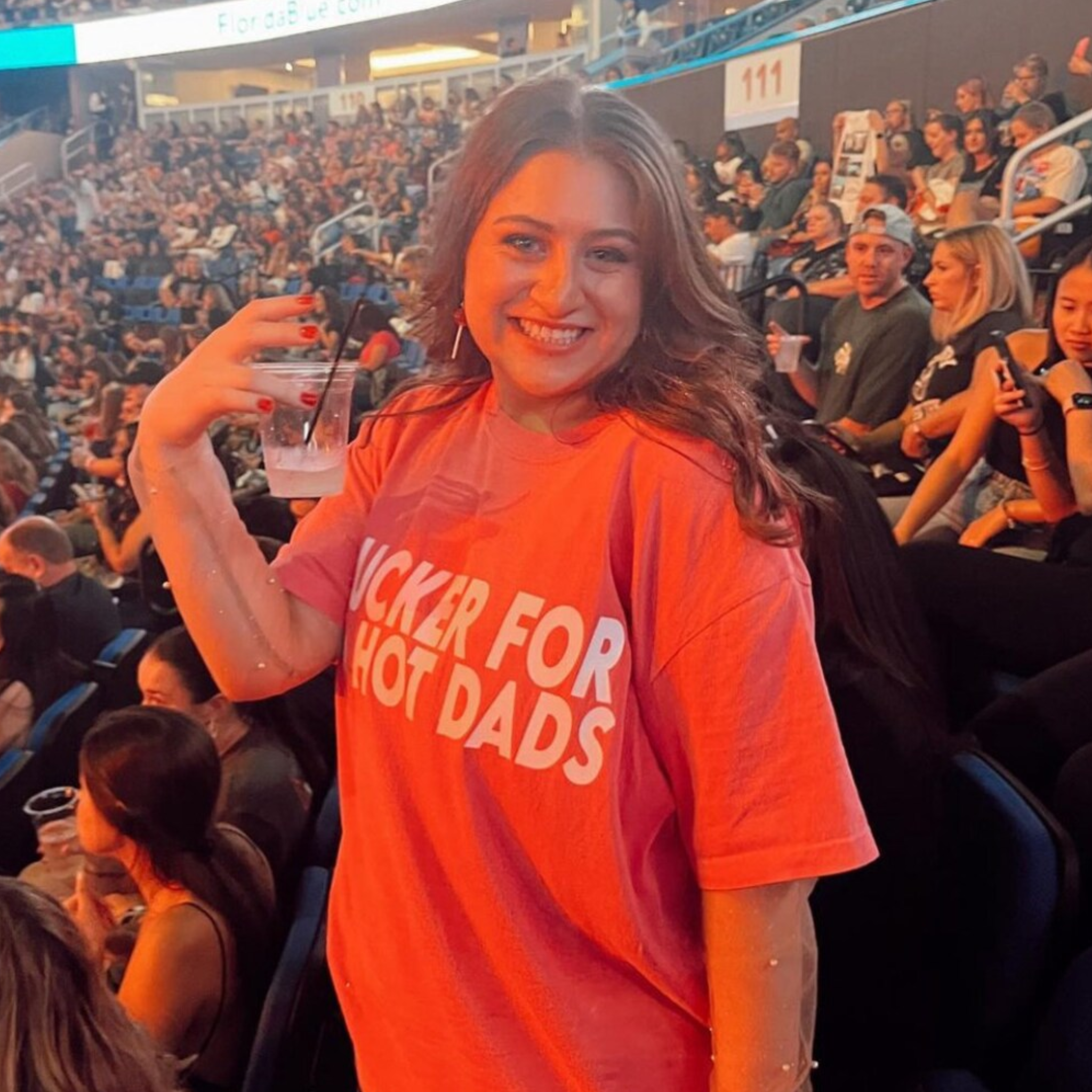 Woman in an oversized pink comfort colors t-shirt that says "sucker for hot dads" 