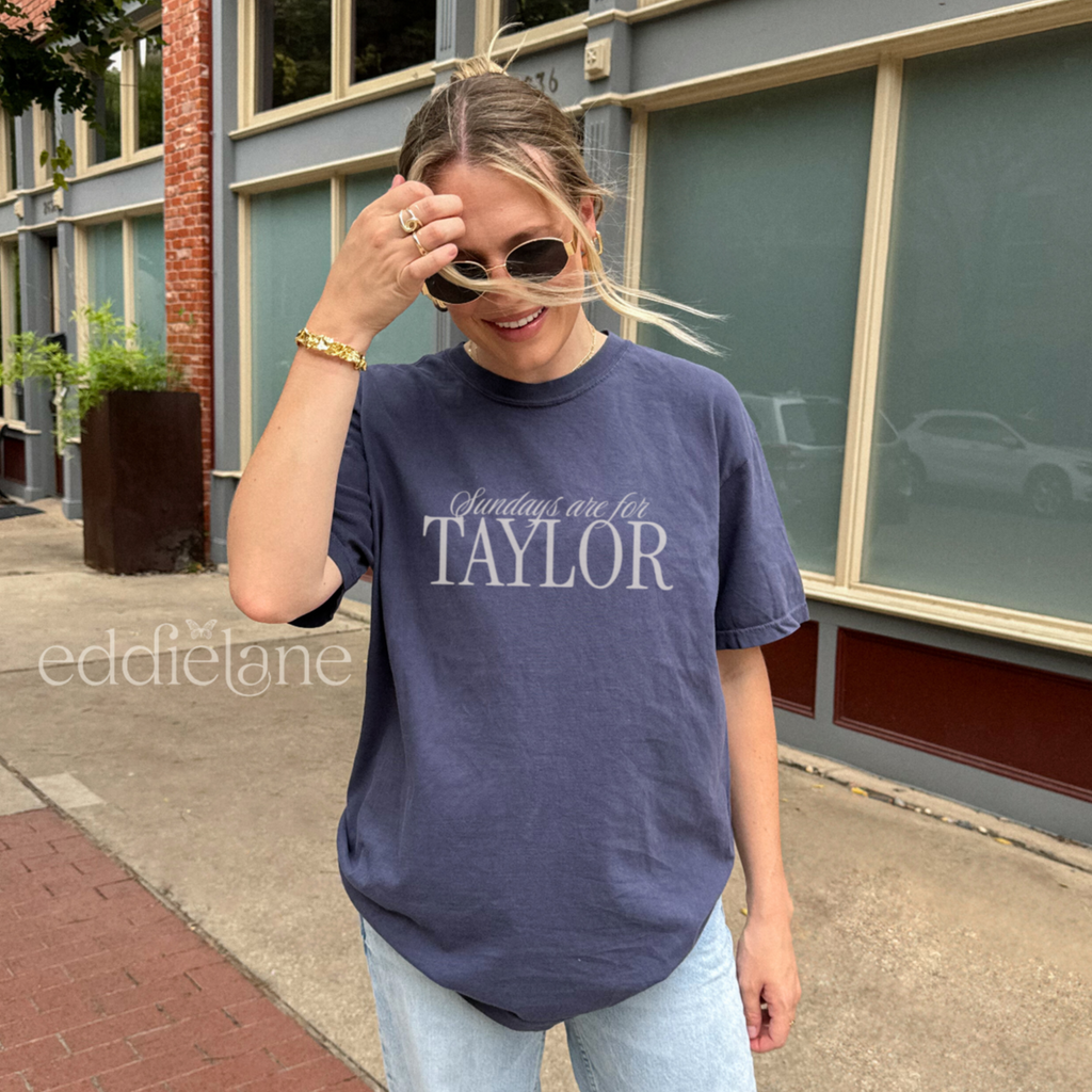 Woman wearing a navy comfort colors t-shirt that says 'Sundays are for Taylor' 