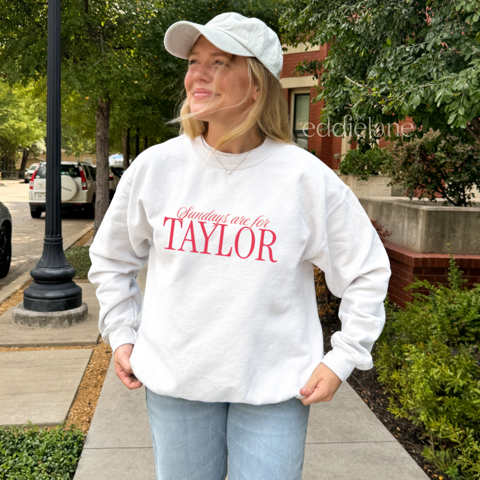 Woman wearing a white crewneck sweatshirt that says 'Sundays are for Taylor' 