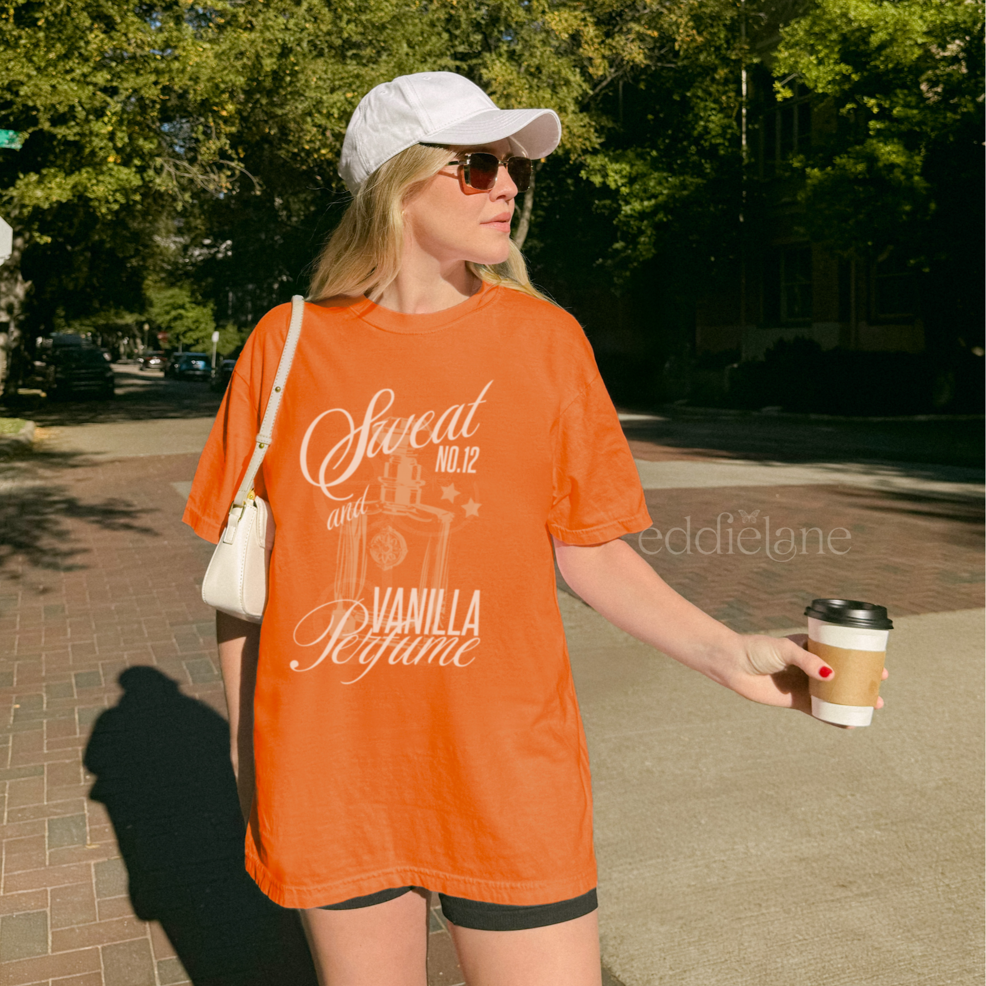 woman wearing an orange comfort colors graphic tee with an illustration of a perfume bottle and the words "sweat and vanilla perfume" 
