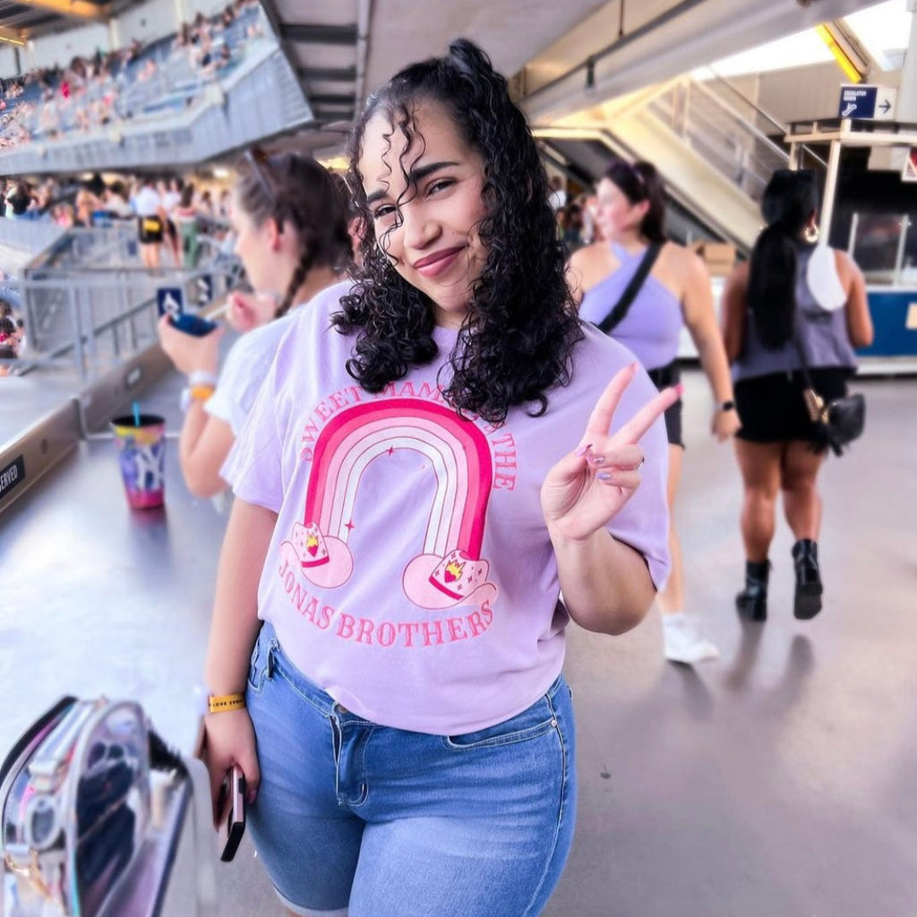 Woman in a light purple graphic tee that says "sweet mama it's the jonas brothers" 