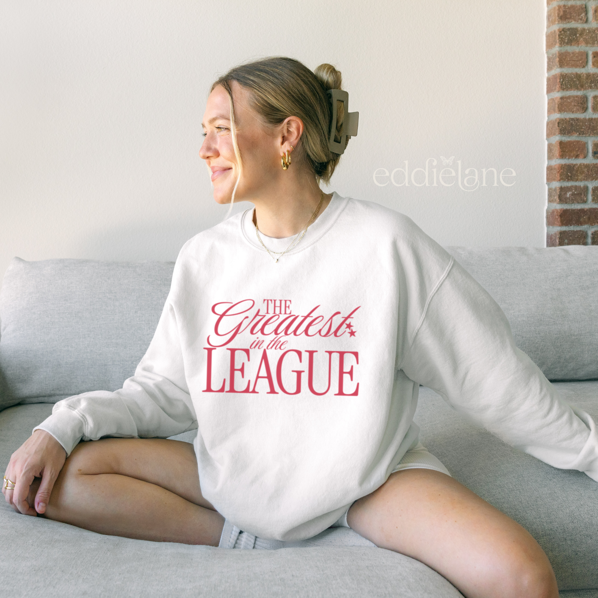 woman in a white crewneck sweatshirt that says "the greatest in the league"