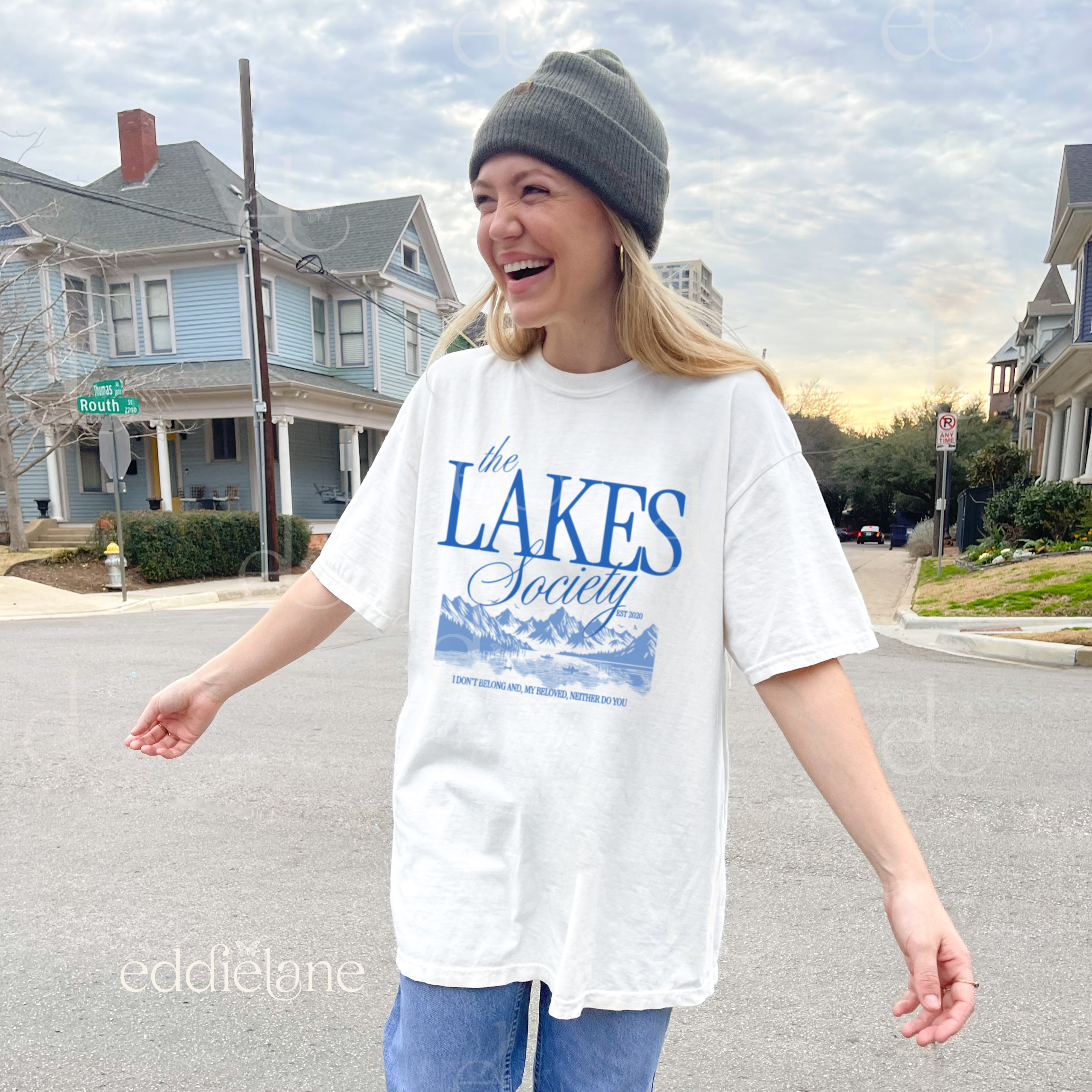 Girl wearing an oversized white graphic t-shirt that says 'The Lakes Society' wth a sketch of a lake surrounded by mountains 
