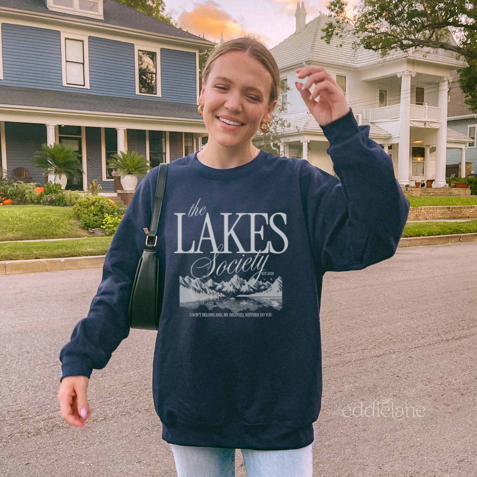 Woman wearing a navy sweatshirt with 'The Lakes Society' design and a silhouette of a lake surrounded by mountains, inspired by the lakes by taylor swift from folklore.
navy the lakes sweatshirt 