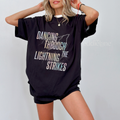 Woman wearing a black oversized t-shirt with the words "dancing through the lightning strikes" and a graphic of a ligtning bolt
