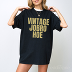 Woman wearing a black oversized t-shirt that says 'Vintage Jobro Hoe' in bold letters in gold.
