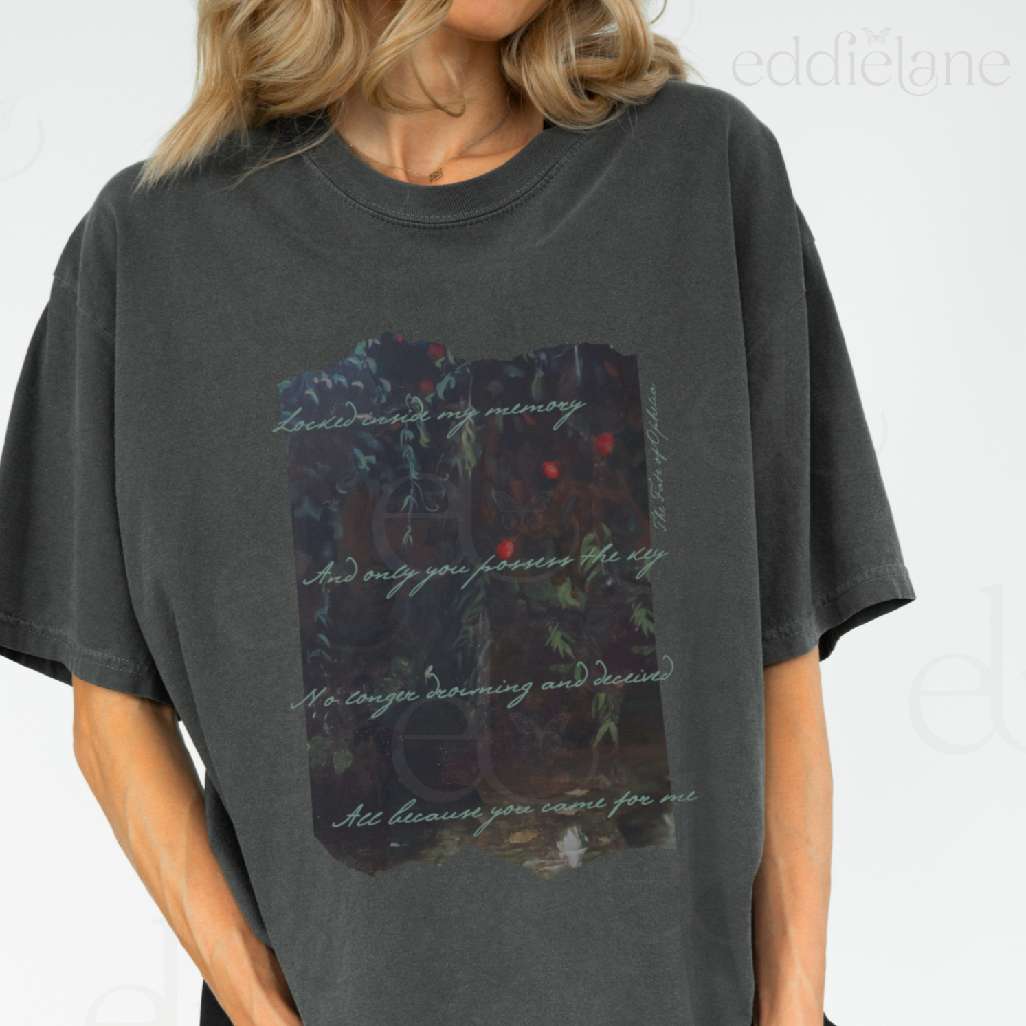 Woman wearing a dark gray t-shirt with a picutre of a painting and the words "Locked inside my memory and only you possess the key no longer drowning and deceived all because you came for me"