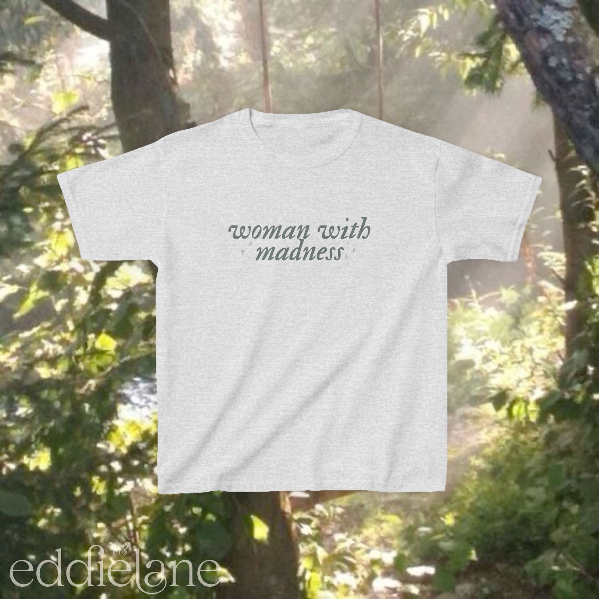Light gray baby tee with words "woman with madness" inspired by the last great american dynasty from folklore by taylor swift.
