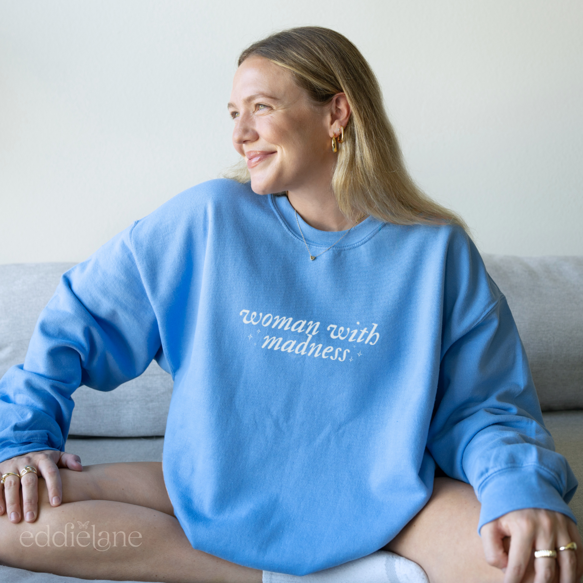woman wearing a carolina blue colored sweatshirt with 'woman with madness' inspired by the last great american dynasty from taylor swift's folklore.
