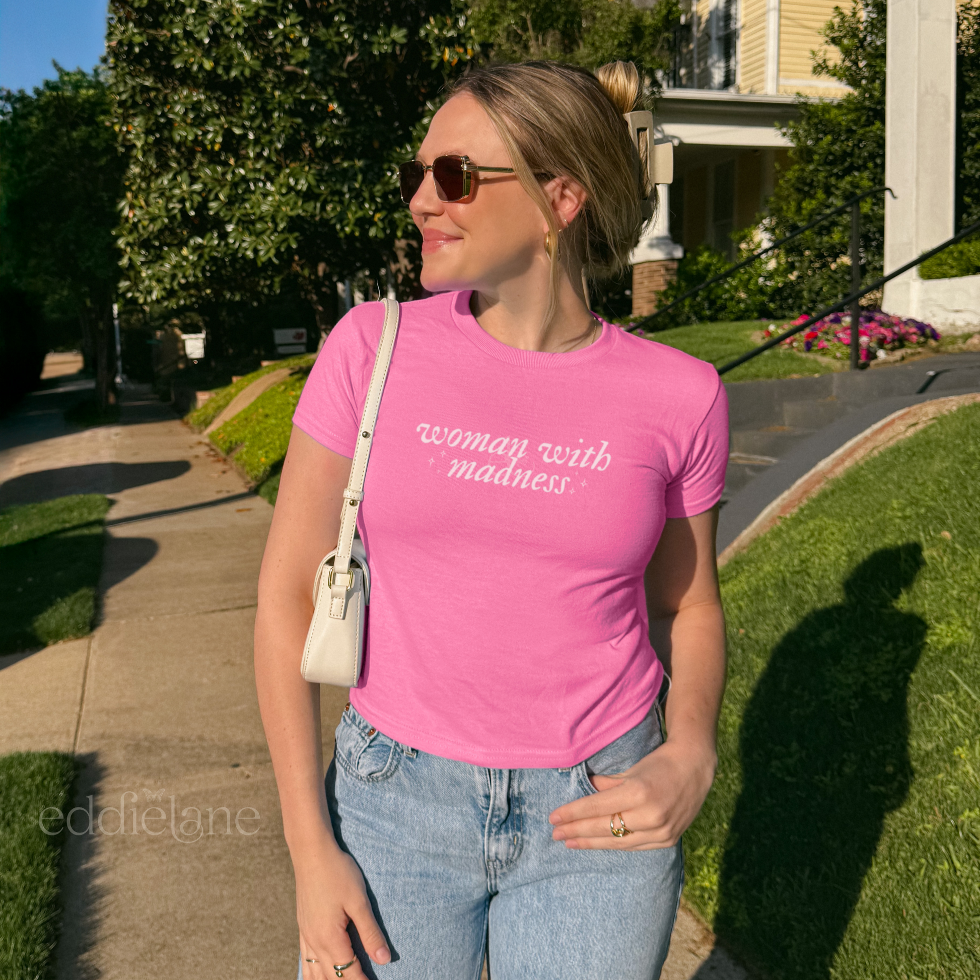 Woman wearing a pink baby tee with words "woman with madness" inspired by the last great american dynasty from folklore by taylor swift.